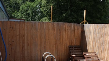A rectangular pool with a metal ladder, surrounded by a wooden deck and a wooden fence.