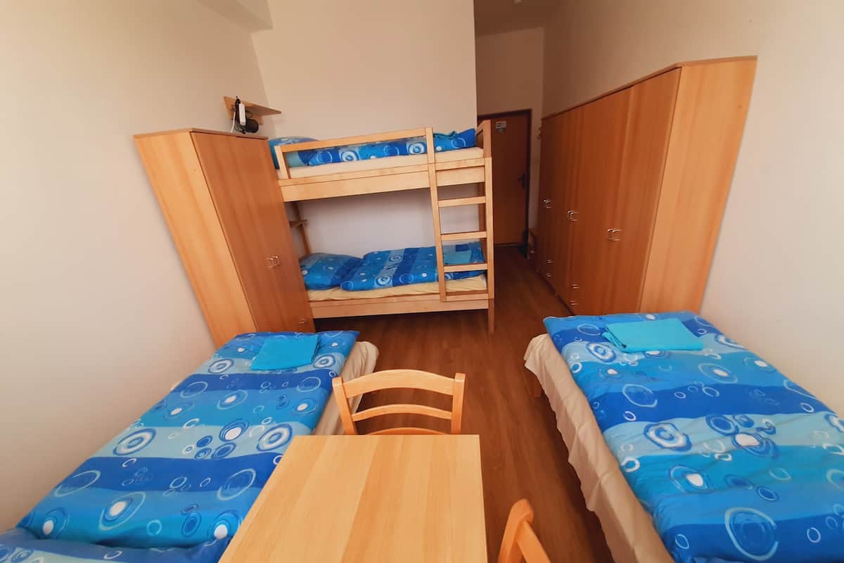A dormitory room with bunk beds, a wooden table, and matching chairs.
