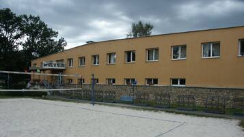 A sandy beach volleyball court adjacent to a building with multiple windows and a sign reading "Sport Hotel 'BK PODIPOU'.