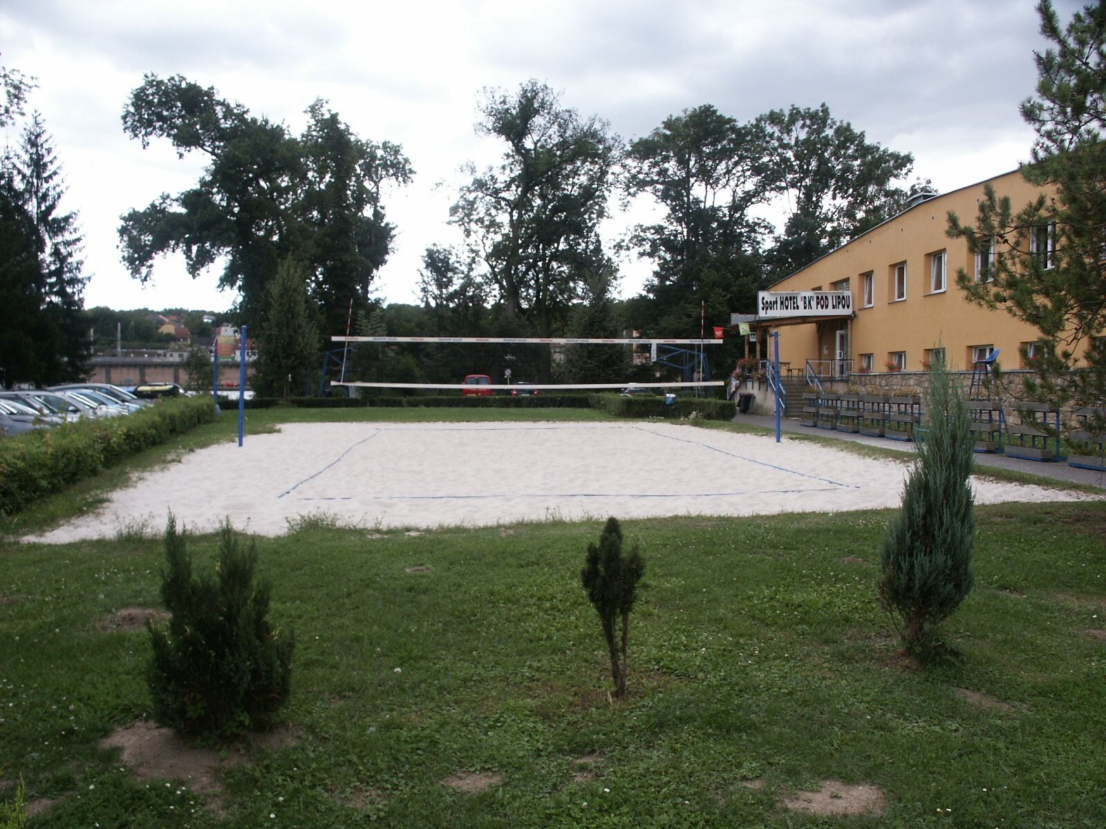 A sports facility with a volleyball net, surrounded by a grassy area and trees.