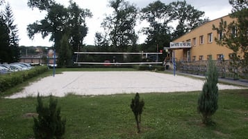 A sports facility with a volleyball net, surrounded by a grassy area and trees.
