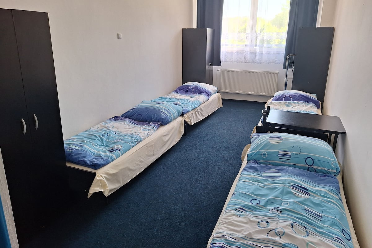 A room with two single beds, a desk, a wardrobe, and a window with curtains.