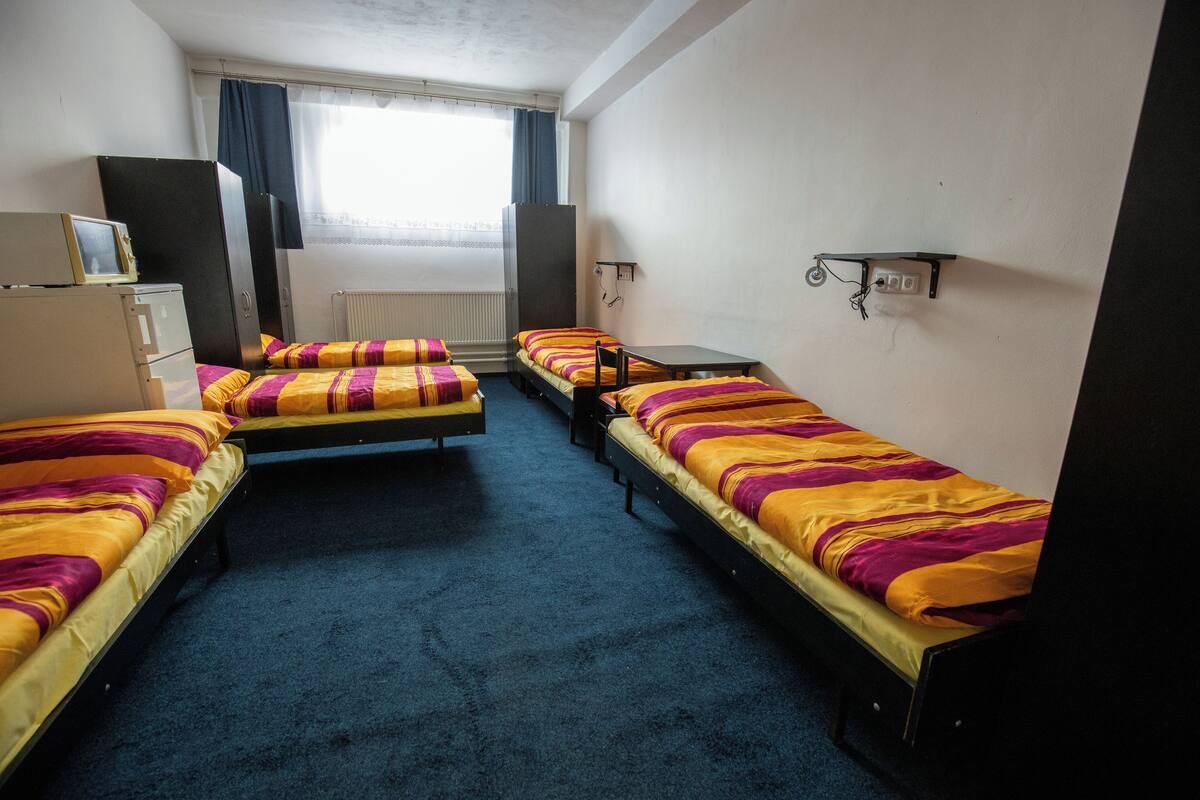 A room with three single beds, a desk, a radiator, and a window with curtains.