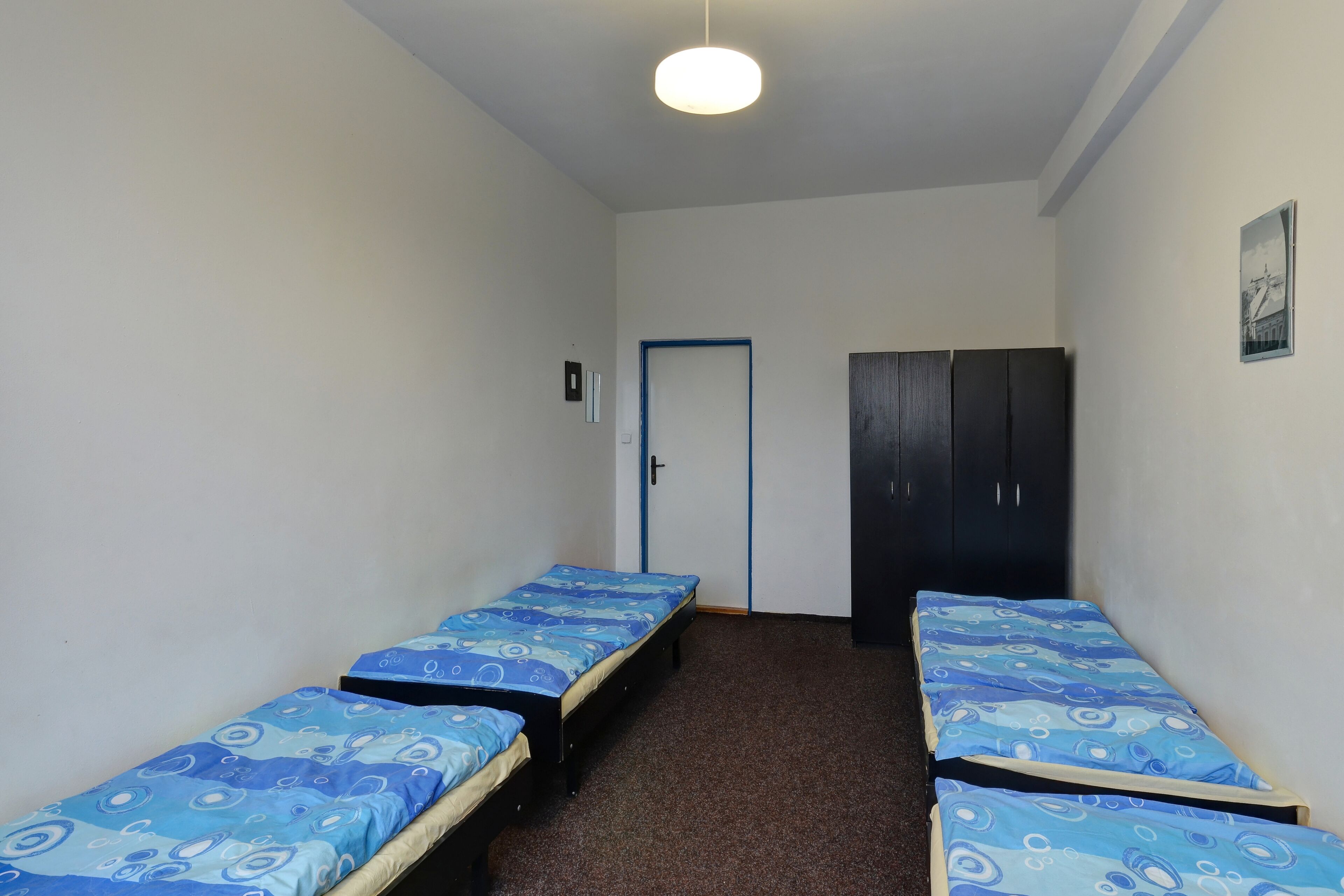 A dormitory room with two single beds, a wardrobe, and a door.