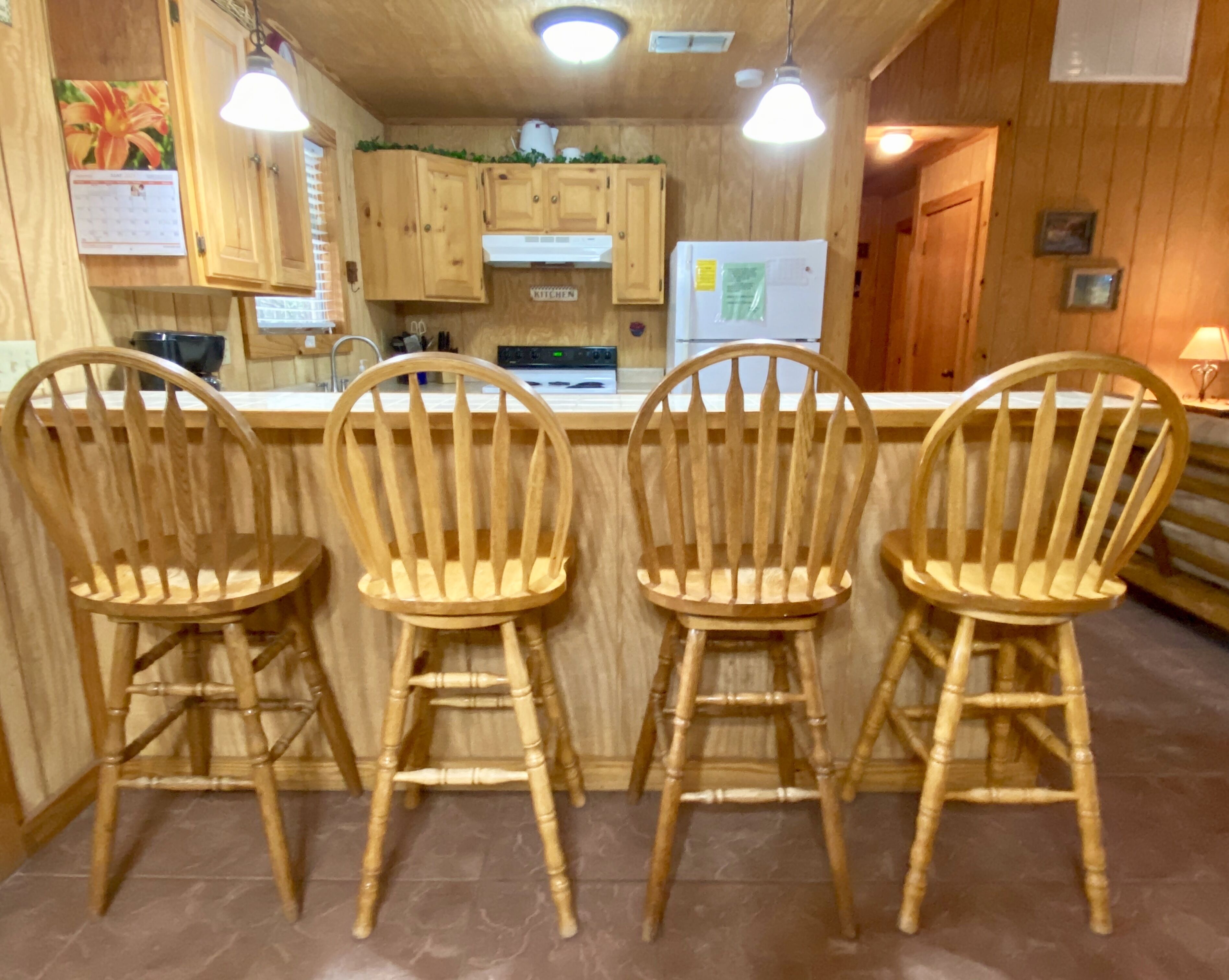 Une cuisine avec des meubles de rangement en bois, un réfrigérateur et trois tabourets de bar en bois.