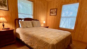 Un dormitorio con una cama grande, paredes de madera y dos ventanas con persianas.