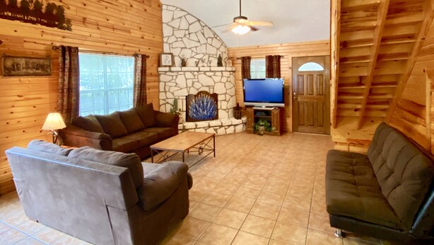 A cozy log cabin interior with a stone fireplace, a television, and a comfortable seating area. - Float 2 Cabin ~ Private Frio River Access @ Comanche Crossing, Cowboy Style! (Concan)