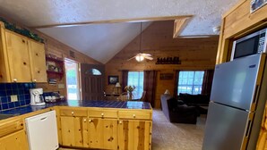 A kitchen with wooden cabinets, a coffee maker, a refrigerator, and a dining area with a table and chairs. - Float 2 Cabin ~ Private Frio River Access @ Comanche Crossing, Cowboy Style! (Concan)