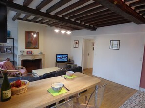 A dining area with a wooden table, chairs, a television, and a fireplace. - Cathedral cottage (Bayeux)