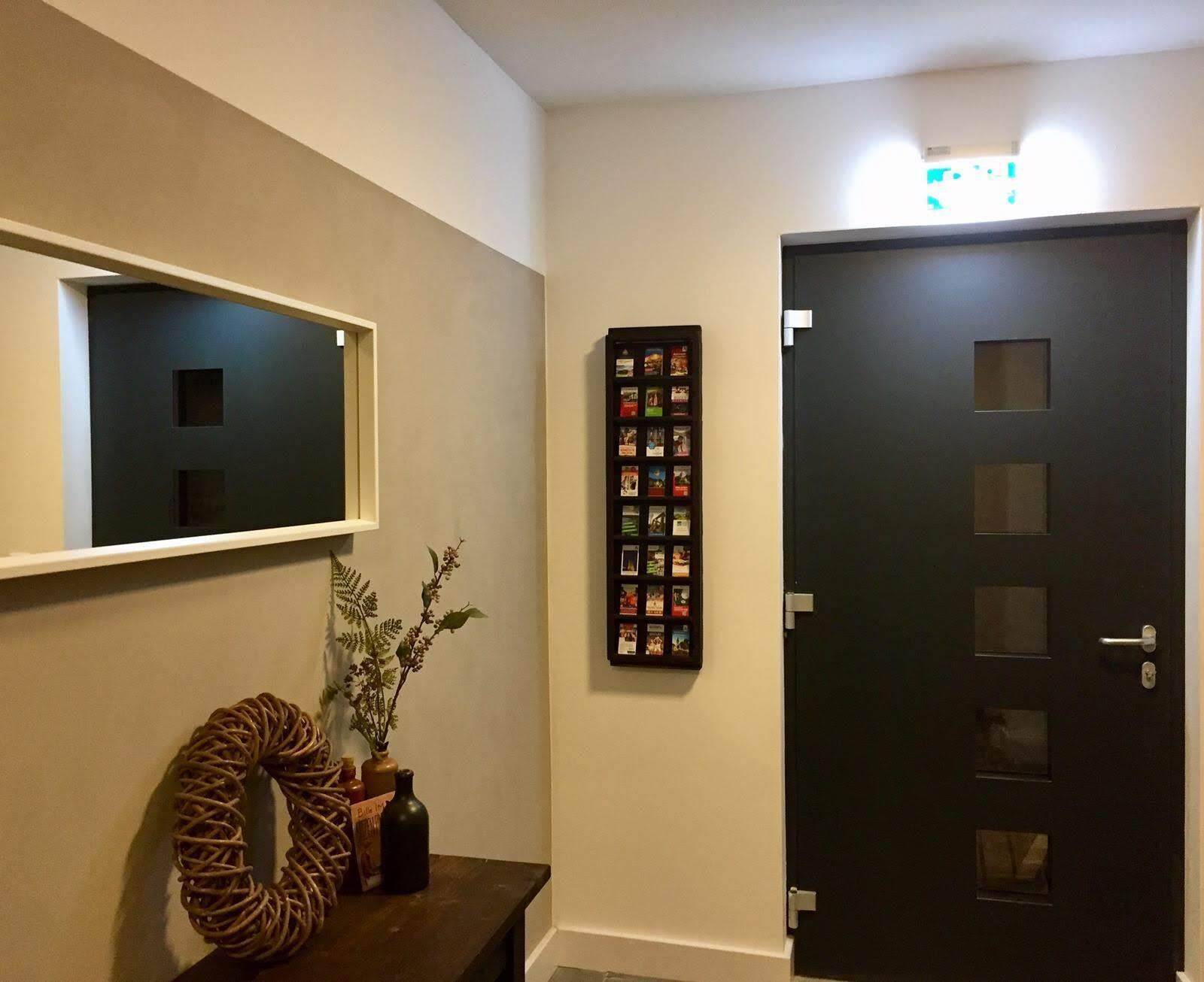 A hallway with a dark door, a wall-mounted photo frame, and a small table with a plant and a decorative item.
