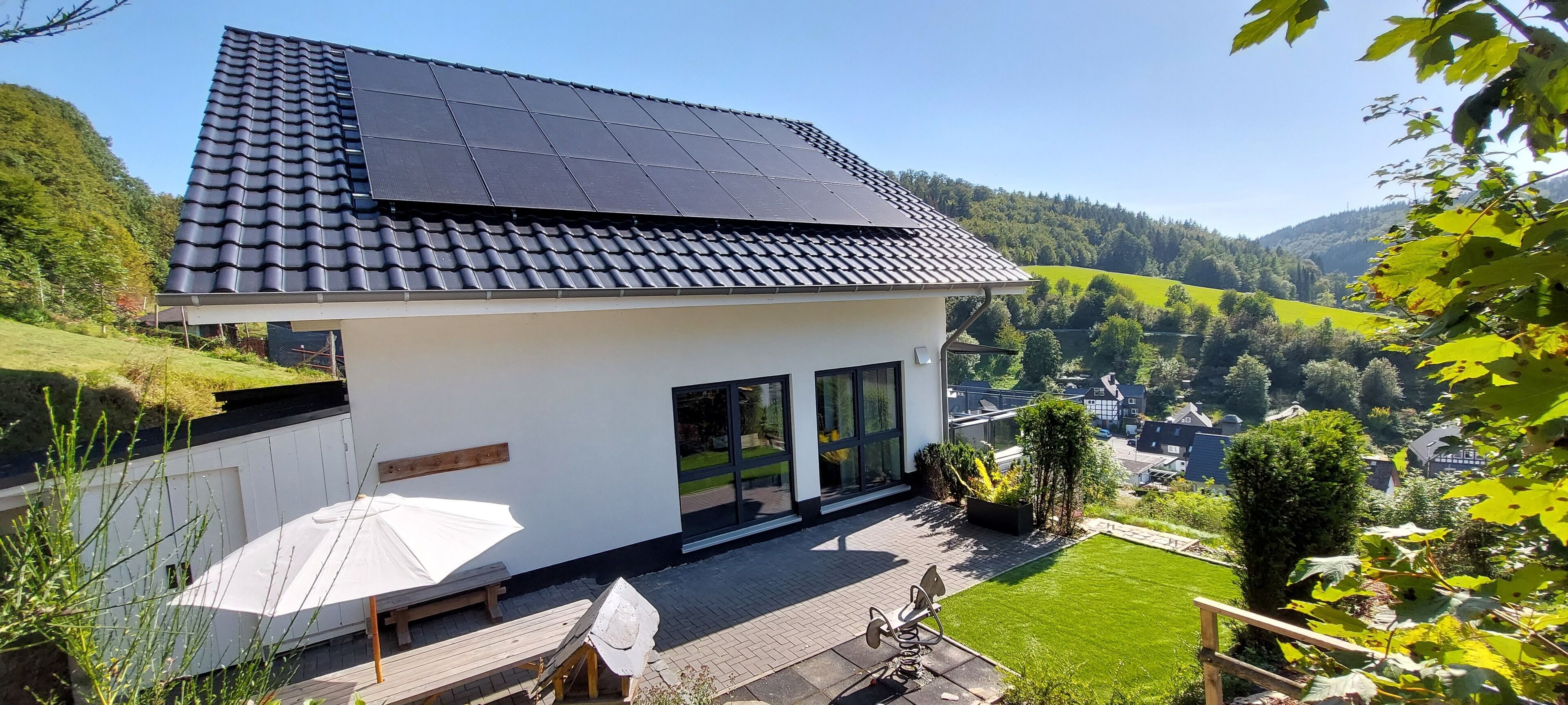 A modern house with a sloped roof, solar panels, and a view of a green valley.