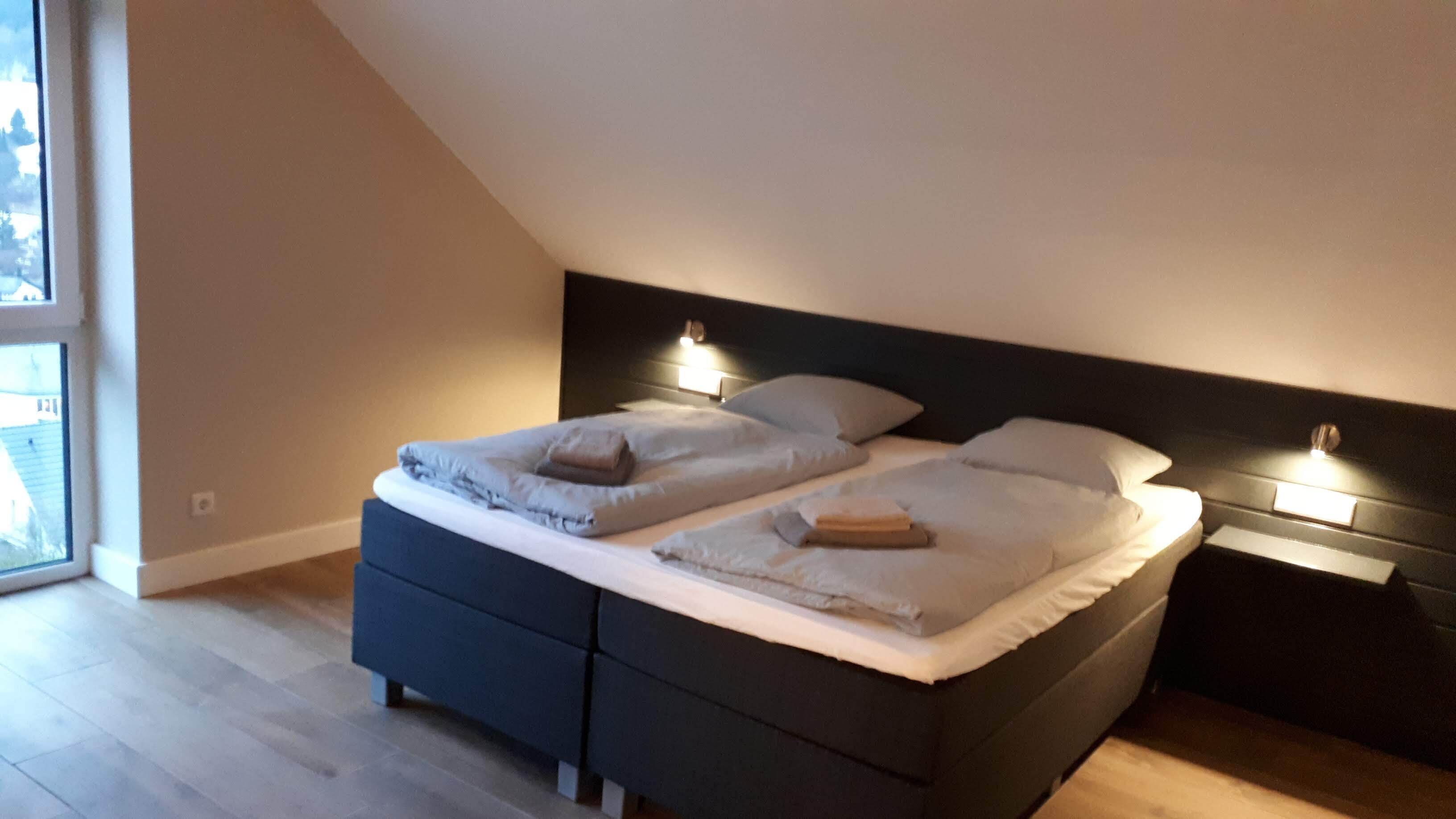 Ein Schlafzimmer mit dunklem Kopfteil, zwei Betten, Nachttischlampen und einem großen Fenster.