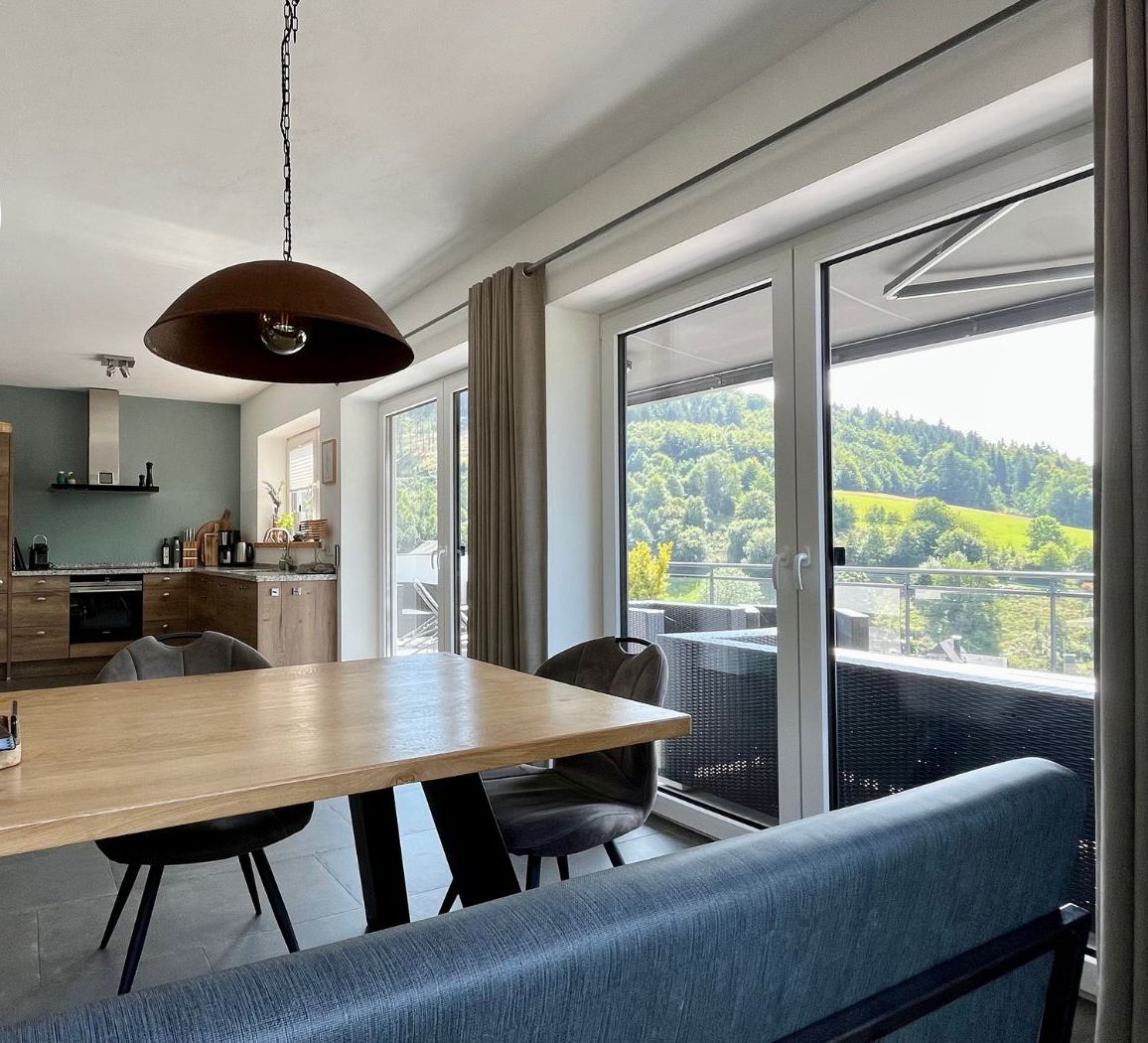 Une cuisine moderne avec un plan de travail en bois, un luminaire suspendu et une vue sur l’extérieur grâce à de grandes fenêtres.