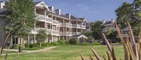 A multi-story hotel with balconies, a well-maintained lawn, and a gazebo.