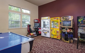 A room with a pool table, arcade games, and a window with blinds.
