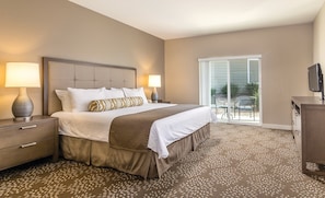 A hotel room with a large bed, two bedside tables with lamps, a flat-screen TV, and a sliding glass door to an outdoor area.
