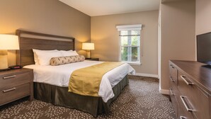 Quarto de hotel com cama, mesas de cabeceira, televisão e janela com persianas.