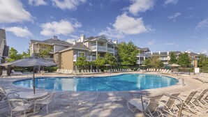 Piscina com espreguiçadeiras e guarda-sóis, cercada por edifícios altos com varandas.