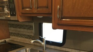 Eine Küche mit Granit Arbeitsplatten, Spüle aus Edelstahl, Holzschränken und einem Fenster über der Spüle.