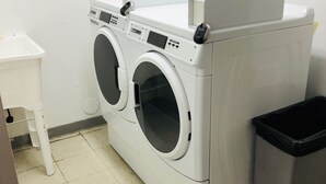 A laundry room with two front-loading washing machines, a small white table, and a trash bin. - Beautiful & Cozy Studio Condo in Denver Tech Center (Greenwood Village)