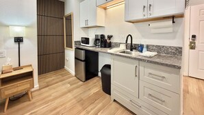 A compact kitchen with a microwave, coffee maker, and sink. There is a wooden cabinet and a black trash bin. - Beautiful & Cozy Studio Condo in Denver Tech Center (Greenwood Village)