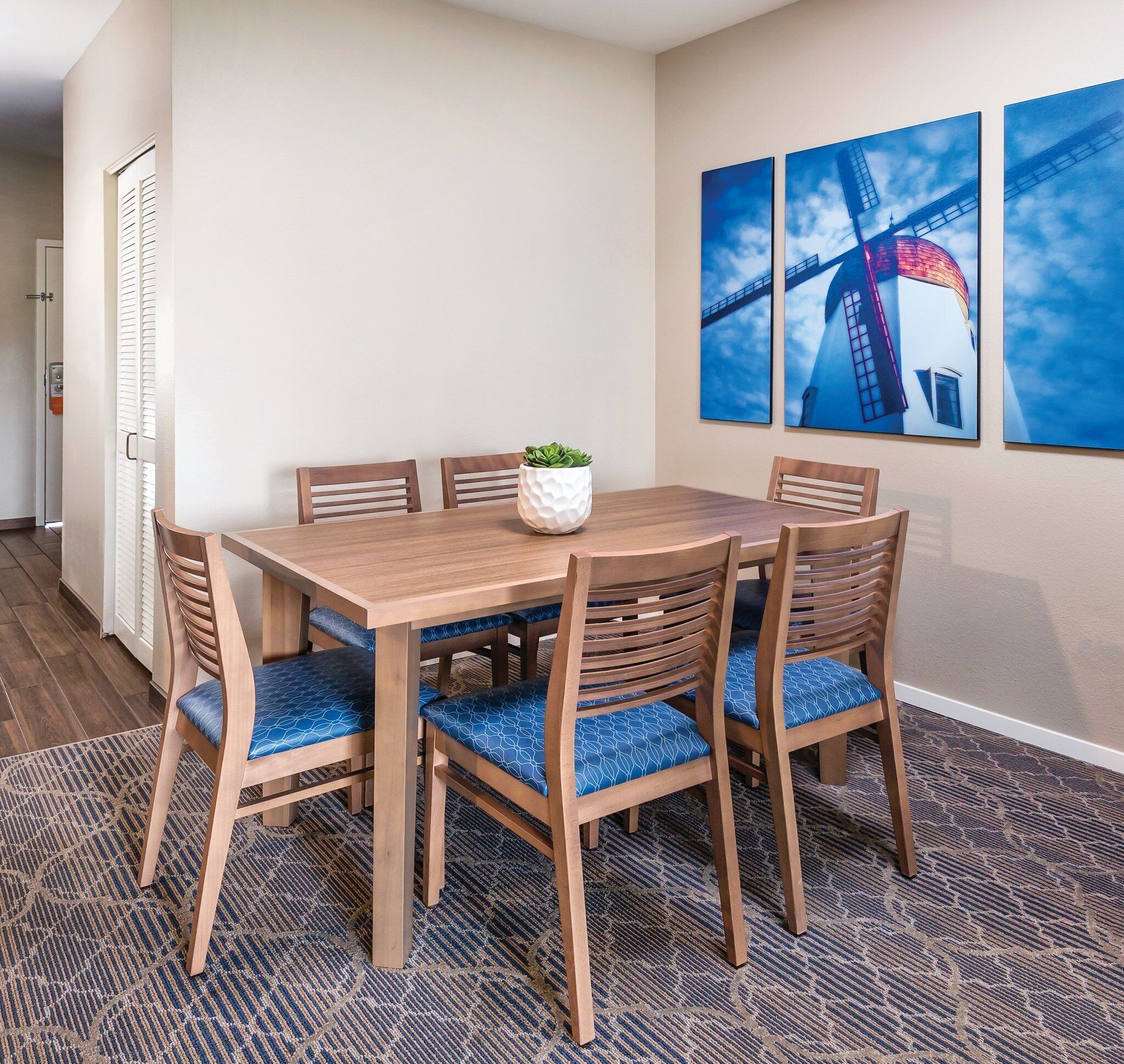 A dining area with a wooden table and chairs, a potted plant, and three framed pictures on the wall.