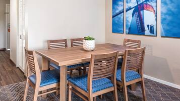 Un coin repas avec une table et des chaises en bois, une plante en pot et trois tableaux encadrés accrochés au mur.