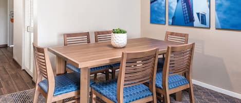 A dining area with a wooden table and chairs, a potted plant, and three framed pictures on the wall.