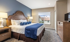 Una habitación de hotel con cama, dos lámparas de noche, televisor, ventana con vistas y cómoda.