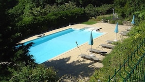 Ein rechteckiger Pool mit gefliestem Sonnendeck, umgeben von Liegestühlen und Sonnenschirmen, inmitten einer üppigen, grünen Landschaft.