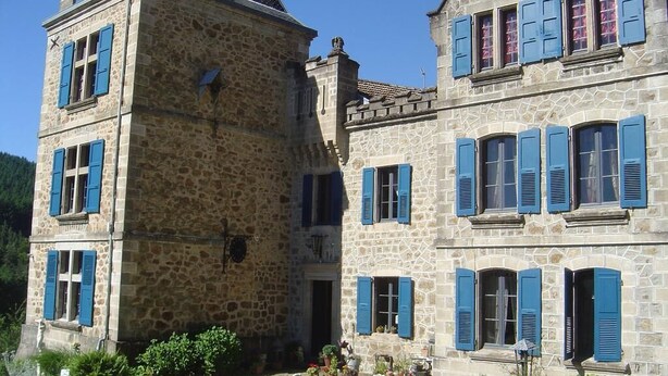 Ein Steinhaus mit blauen Fensterläden, ein Innenhof mit Pflanzen und einer kleinen Fontäne.
