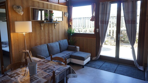 A cozy room with a wooden interior, a sofa, a table with a patterned tablecloth, and a view through a glass door. - Seasonal rental apartment for up to 4 people (Bussang)