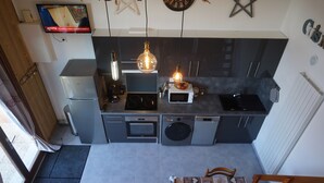 A compact kitchen with a dining area, featuring a built-in oven, microwave, and washing machine. - Seasonal rental apartment for up to 4 people (Bussang)