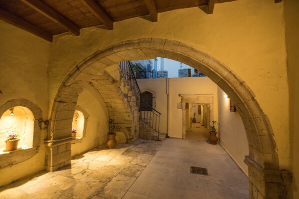 An arched corridor with stone walls, potted plants, and a staircase leading to an upper level.