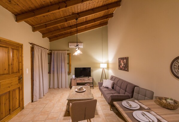 Ein Wohnzimmer mit Holzboden, einem Fernseher, einem Sofa, einem Esstisch gedeckt mit Tellern und Besteck sowie einer Lampe.