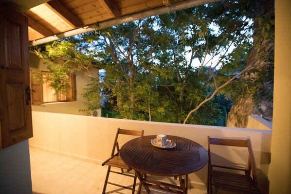 A wooden table and chairs on a balcony with a view of trees and a building in the background.