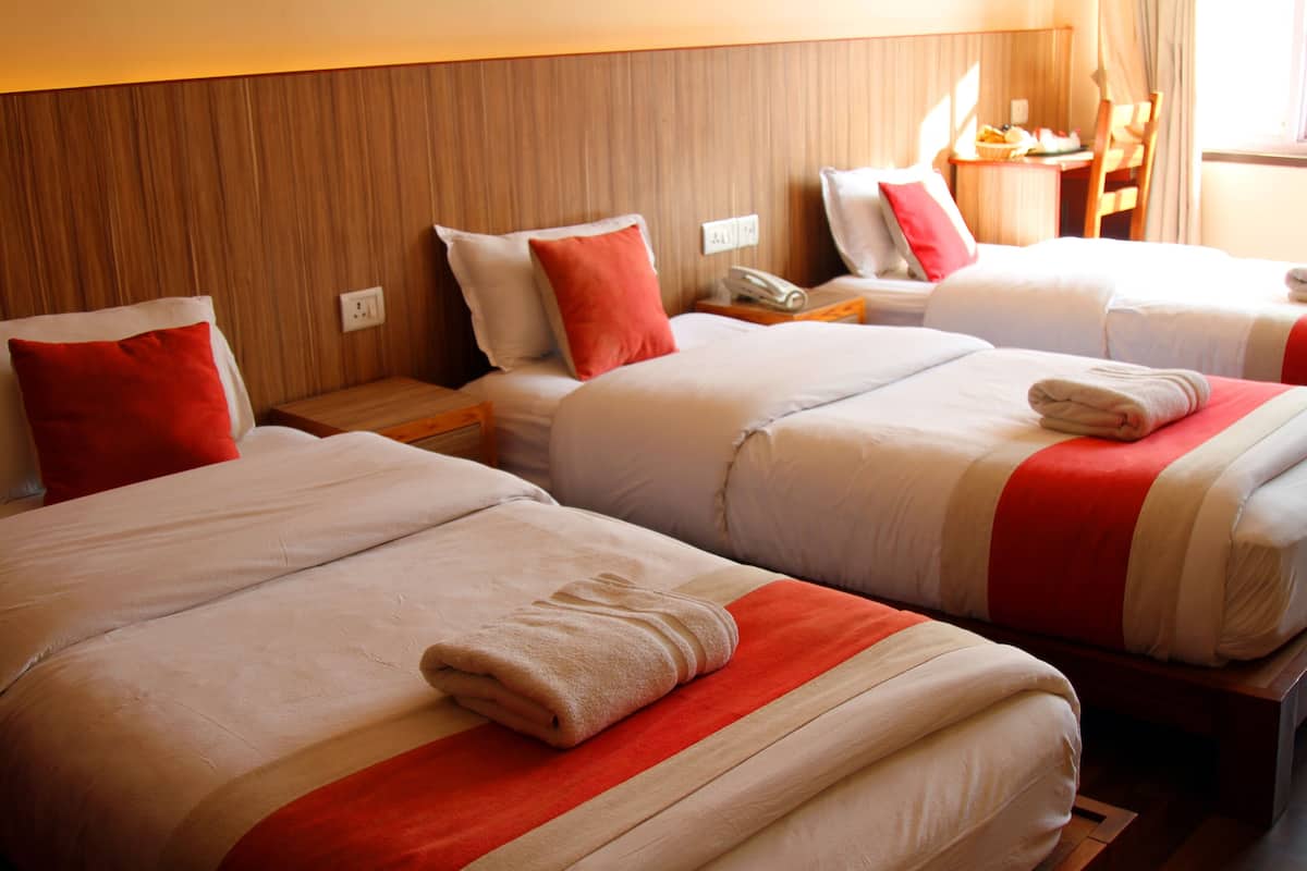 Habitación de hotel con tres camas, cada una con colcha roja y blanca y cabeceros de madera.