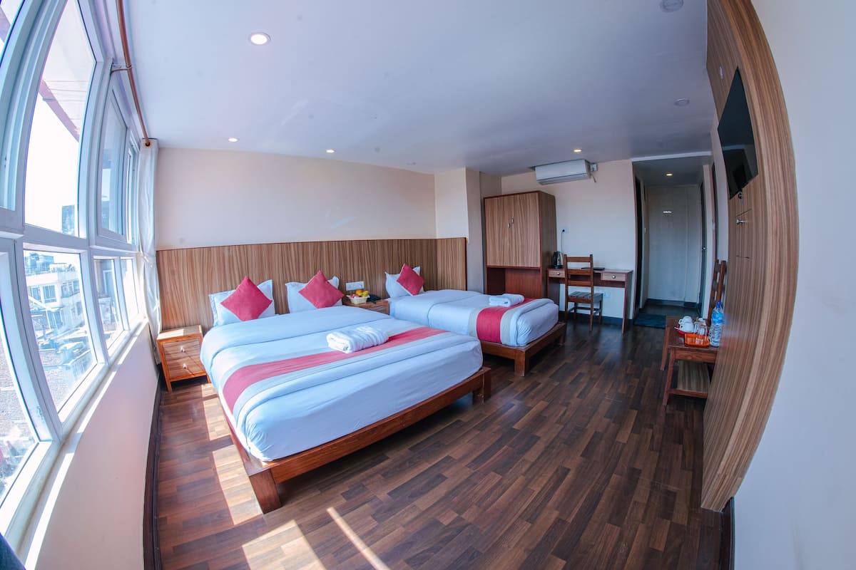 Habitación de hotel con dos camas, piso de madera, un ventanal grande y un televisor fijado a la pared.