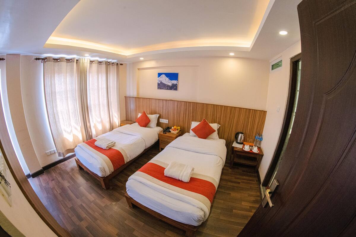 Una habitación de hotel con dos camas, suelo de madera, una mesita de noche con lámpara y un cuadro en la pared.