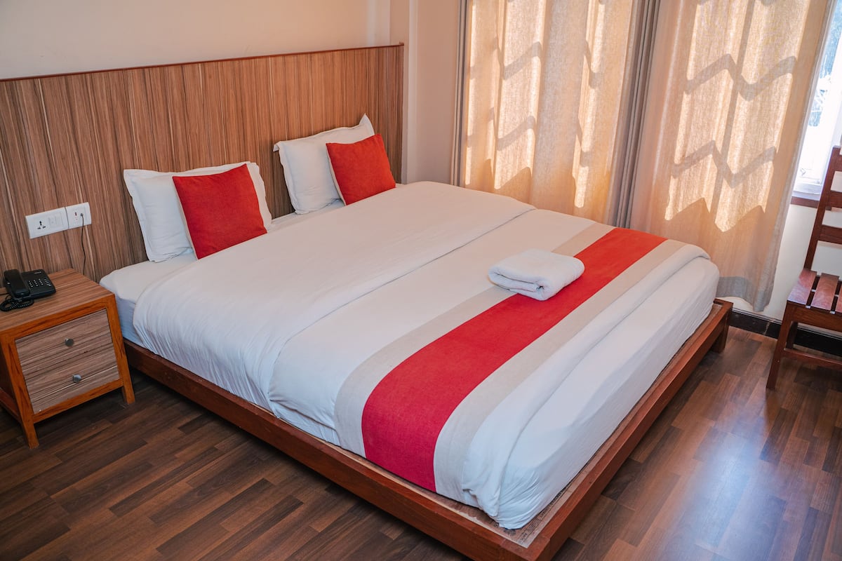 Una cama bien hecha con cabecera de madera, una mesita de noche con un teléfono y una ventana con cortinas.