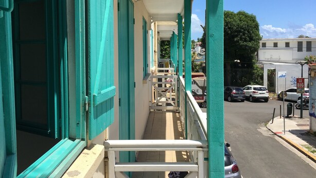 A building with teal shutters and a balcony overlooking a street.