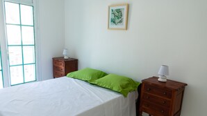 A bedroom with a bed, a nightstand, a drawer, a lamp, and a framed picture on the wall.