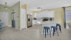Cocina moderna con armarios blancos, refrigerador de acero inoxidable y una isla central con taburetes de bar.