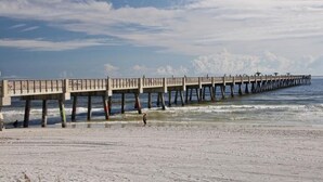 Un muelle se adentra en el océano, con una playa arenosa al frente.