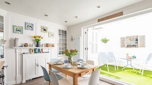 Un espace de salle à manger lumineux, avec une table en bois et des chaises blanches, entouré de meubles blancs et d’œuvres d’art.