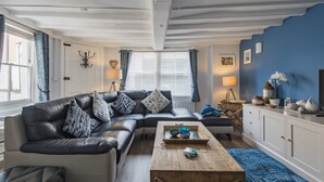 Un salon avec un canapé en cuir noir, une table basse en bois et un tapis à motifs bleus.