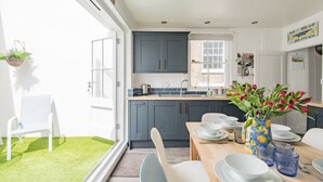 Une cuisine moderne avec des meubles gris, une table à manger dressée avec de l’assiette blanche et de la verrerie bleue, et une fenêtre donnant sur une pelouse verdoyante.