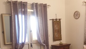 Una habitació amb un llit, una taula de cafè de vidre, un armari de fusta, un mirall i un ventilador de sostre.