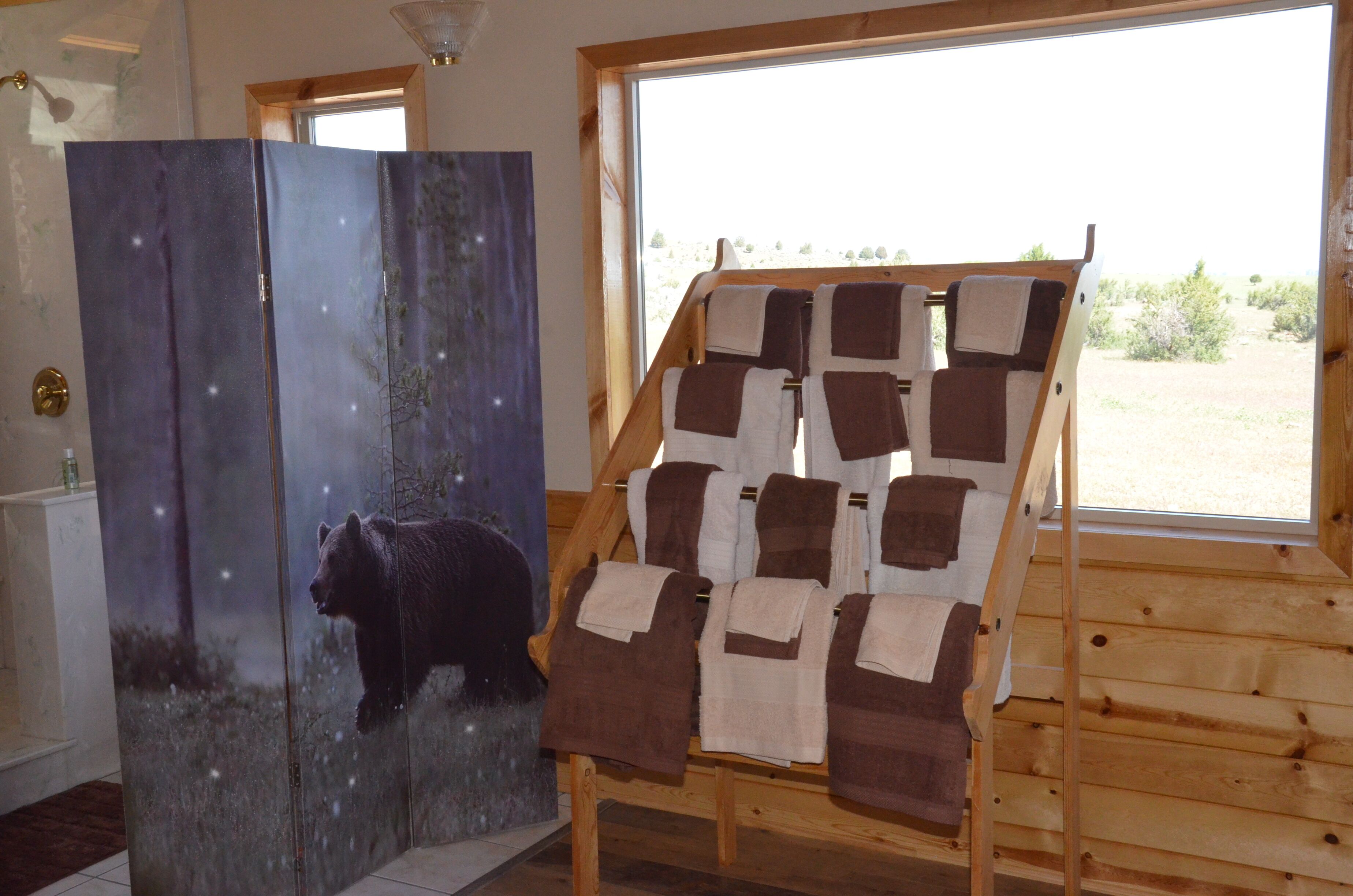 A room with a large window, a wooden bench with towels, and a painting of a bear.