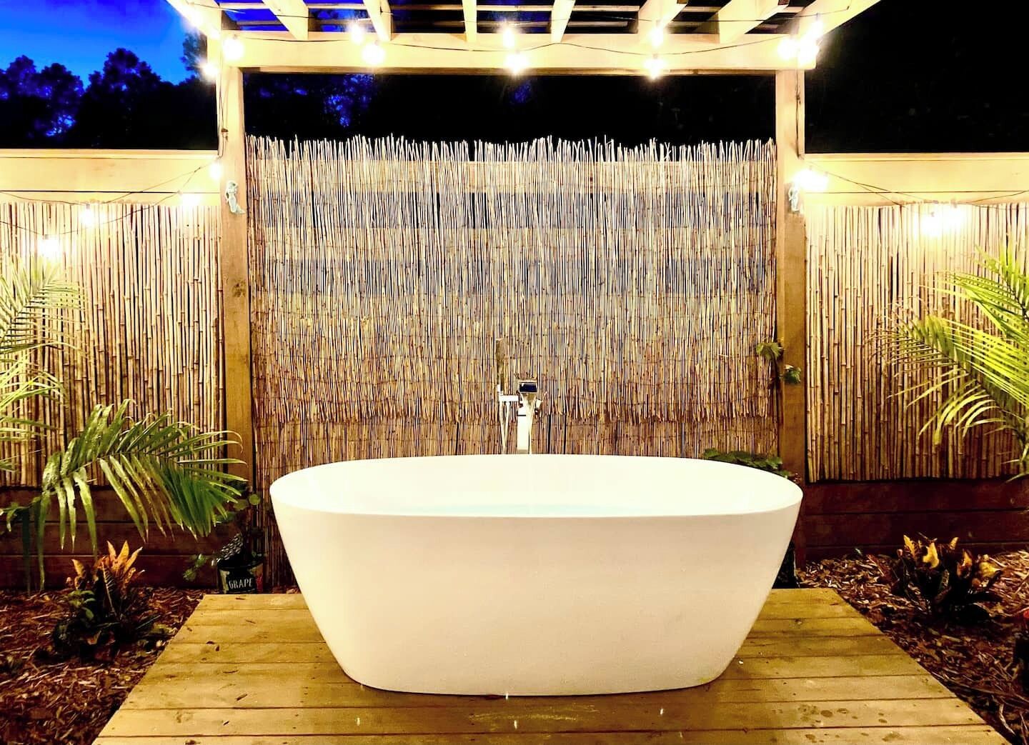 A large outdoor bathtub with a bamboo backdrop and string lights.